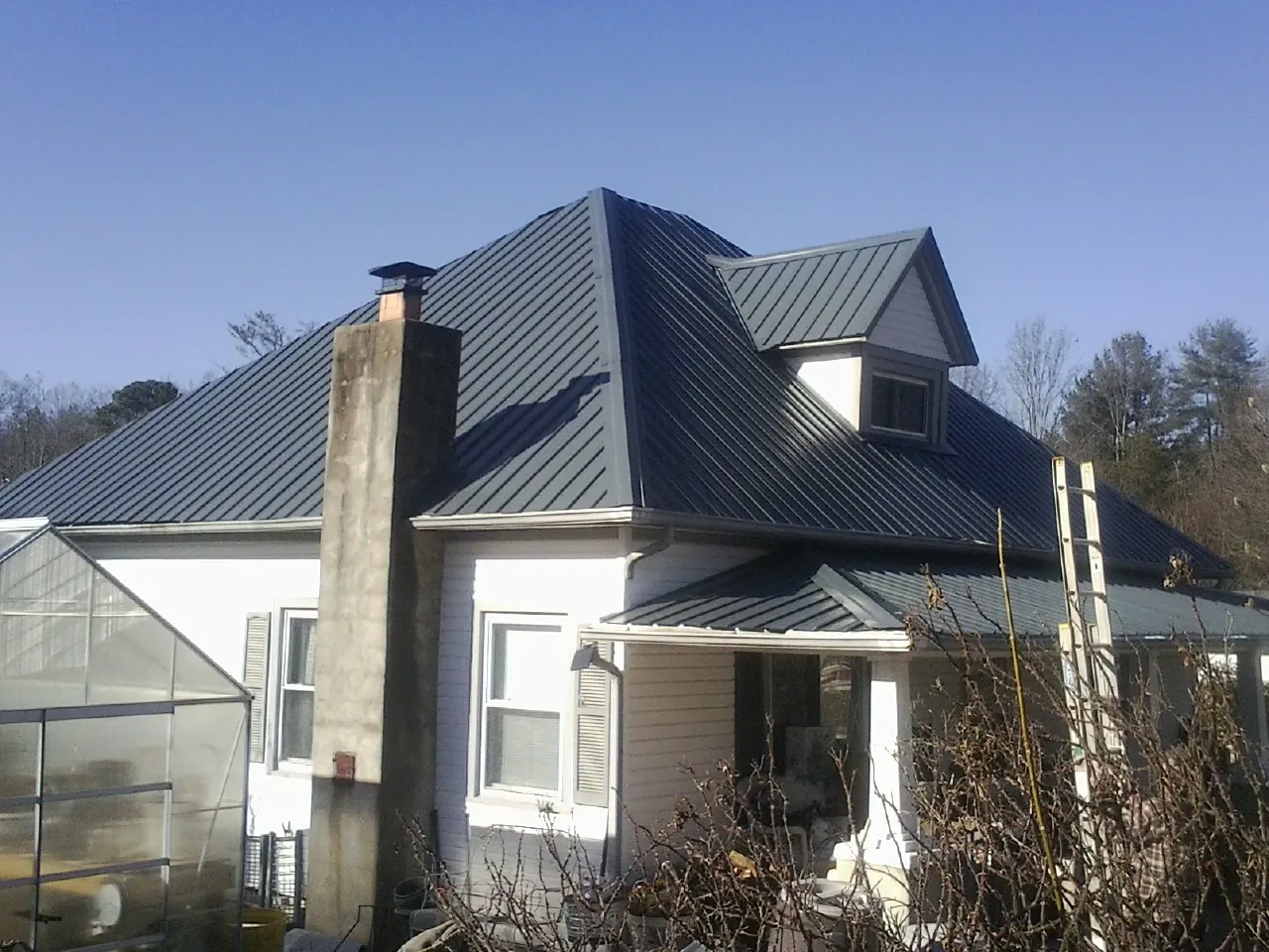 Dark blue standing seam metal roof on a white farmhouse with dormer — Slate & Tile Roof Repair by Roofing Brothers in Pineville