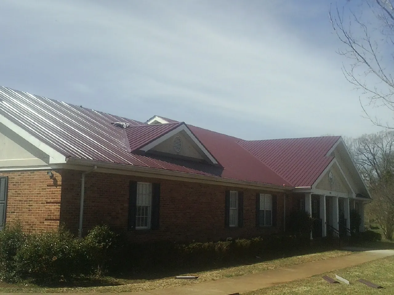 Red metal roof with gabled entries on a long brick building, from a Hail Damage Roof Repair job in Pineville