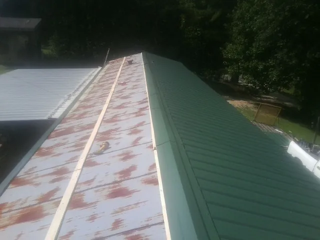 Old rusted panels beside newly installed green metal roofing — Wind Damage Roof Repair by Roofing Brothers in Pineville